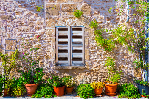The facade of an old stone house with wooden brown shutter and flowerpots. Majorca. Spain.