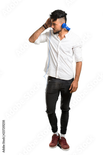 A full-length shot of a Arabic young man with white shirt listening to music with headphones on isolated white background © luismolinero