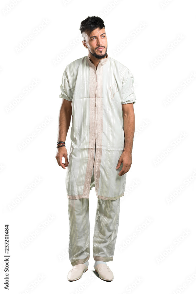 Fototapeta premium A full-length shot of a Arabic young man wearing typical arab clothes having doubts and with confuse face expression on isolated white background