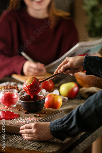Woman dipping apple into bowl with caramel on wooden table