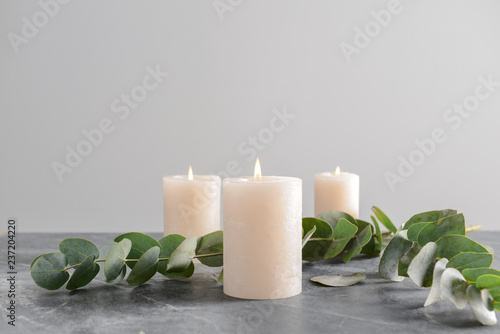 Burning candles with eucalyptus branches on grey table