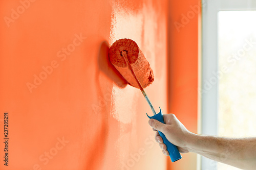 Fototapeta Naklejka Na Ścianę i Meble -  Male hand painting wall with paint roller. Painting apartment, renovating with red orange color paint