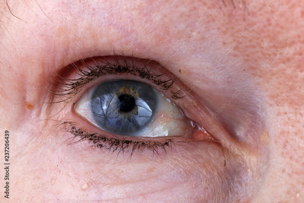 Fototapeta premium Eye and eyelashes with lumps of black ink from an old elderly woman Macro