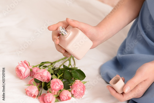 Woman with bottle of perfume on bed at home
