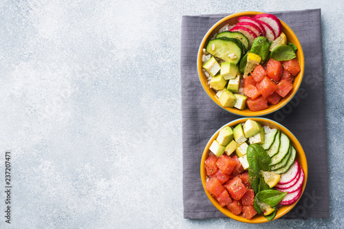 Traditional Hawaiian Poke salad with salmon, avocado rice and vegetables in a bowl on two persons. Top view Copy space
