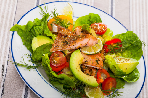 Delicious salad of fried trout, avocado, tomatoes and herbs at plate