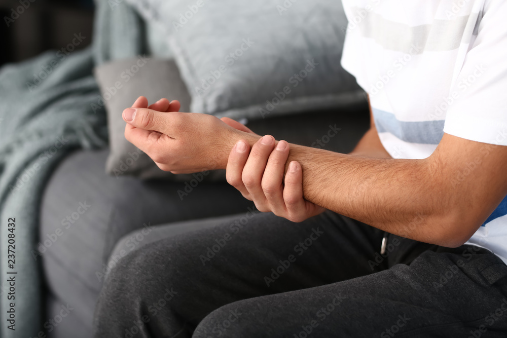 Fototapeta premium Young man suffering from pain in wrist at home, closeup