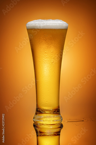 glass of beer on yellow background with reflection