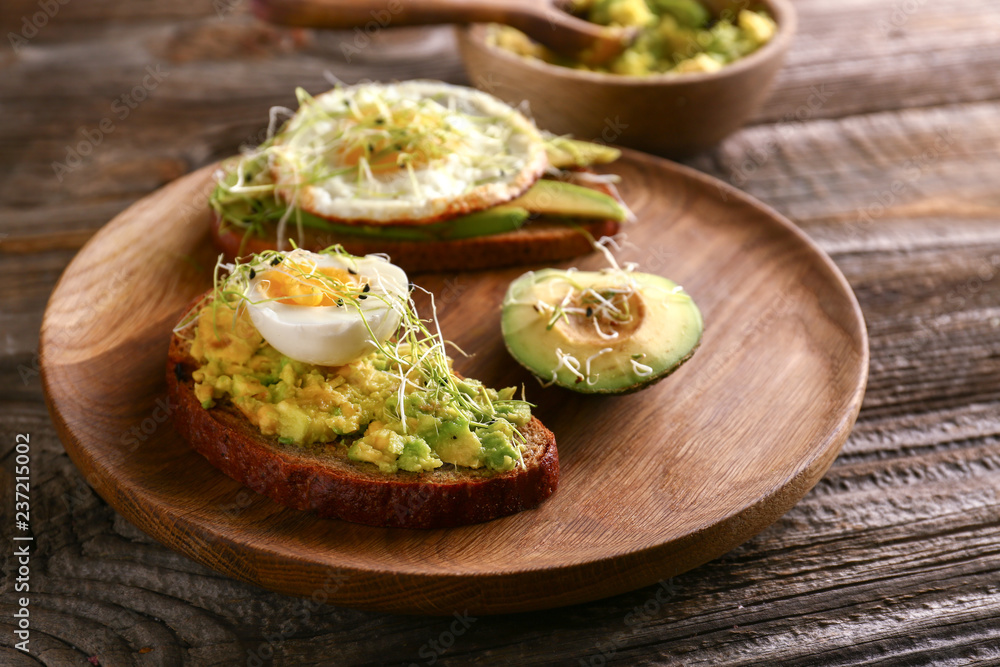 Wooden plate with delicious avocado toasts on table, closeup