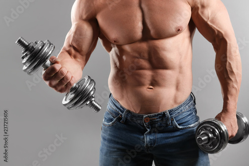 Muscular bodybuilder with dumbbells on grey background