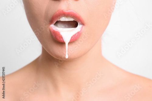 Young woman with white liquid dripping from her mouth on light background. Erotic concept photo
