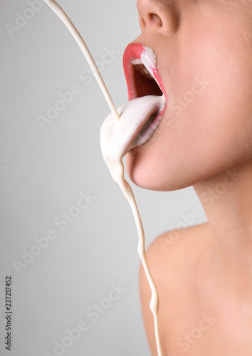 White liquid dripping into woman's mouth on light background. Erotic concept photo