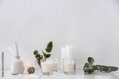 Beautiful composition with burning candles on table near white wall