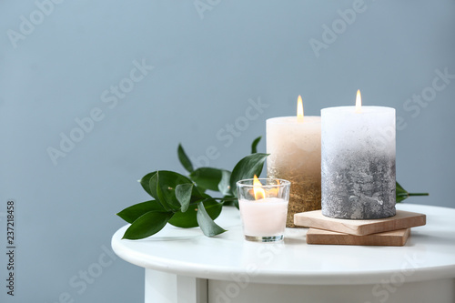 Beautiful composition with burning candles on table near color wall