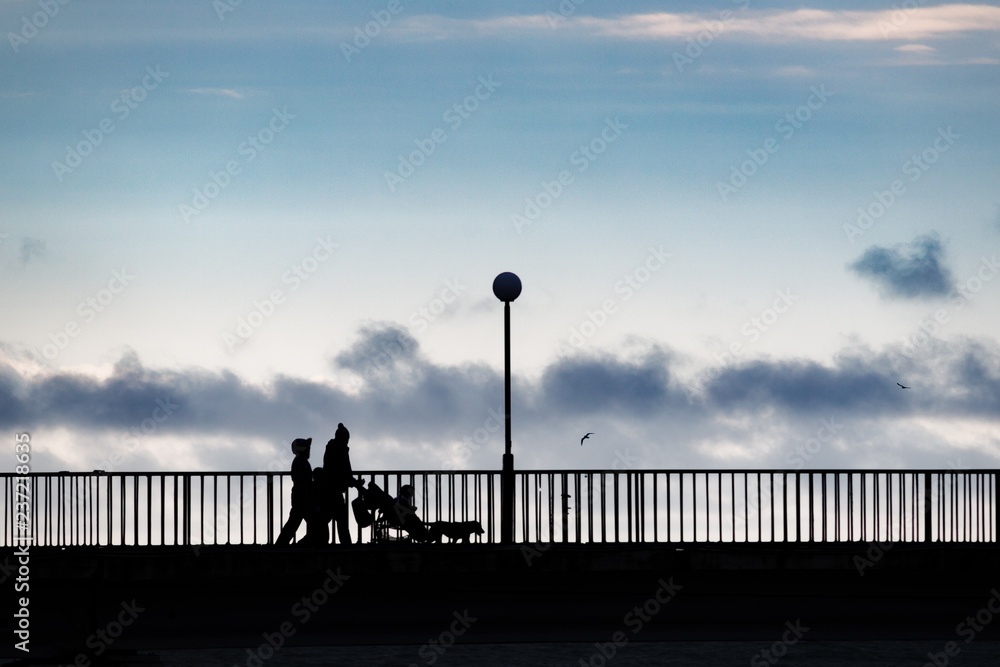 People in silhouette standing on a bridge over a sea