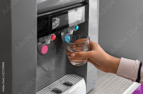Woman filling glass from water cooler, closeup