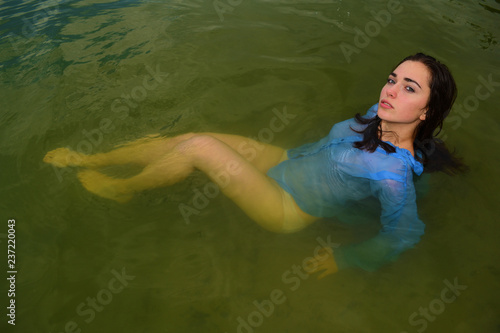 Young sexy naked brunette girl in blue shirt on lake in water.