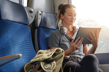 Young woman travelling by train with tablet and headphones
