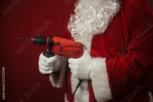 Santa Claus holding using electric drill ready to renovate space background. Handyman repairman in festive mood for seasonal business work. Merry Christmas and Happy New Year time.