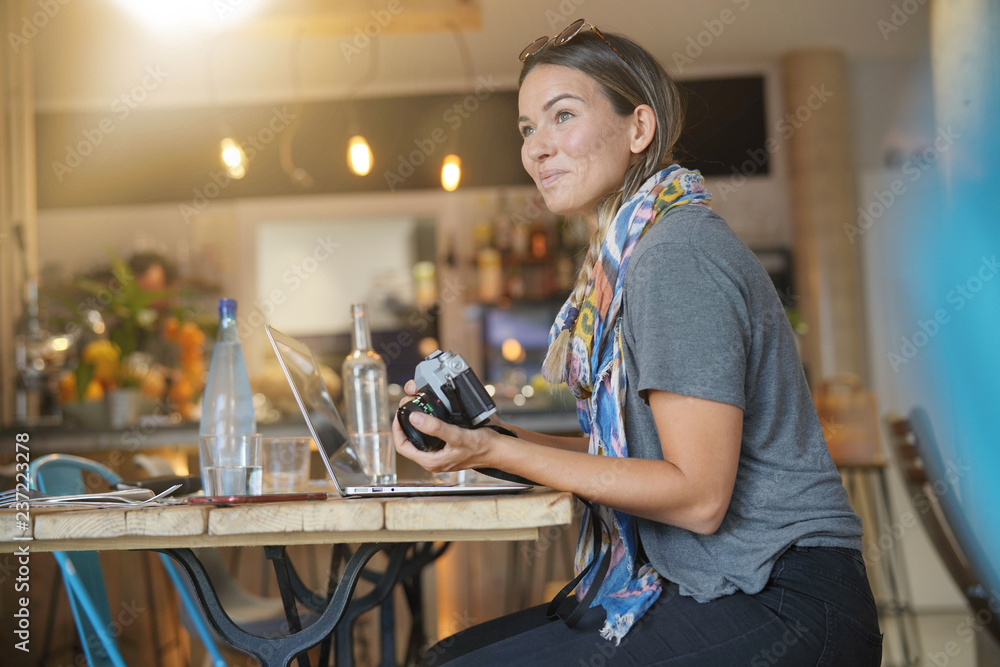 Young woman in coffee shop with camera and laptop Young woman in coffee shop with camera and laptop