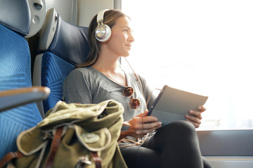 Young woman travelling by train with tablet and headphones