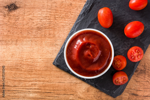 Ketchup sauce in bowl and tomatoes on wooden table. Top view

