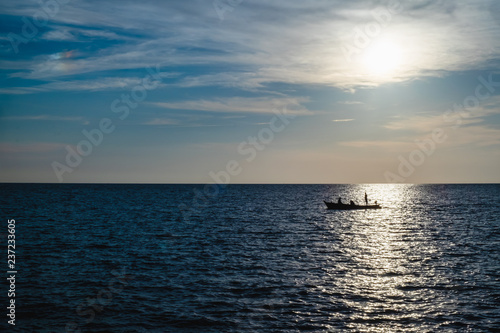 Silhouette of a fisherman on fishing boat with the sea and blue sky © Attaphon
