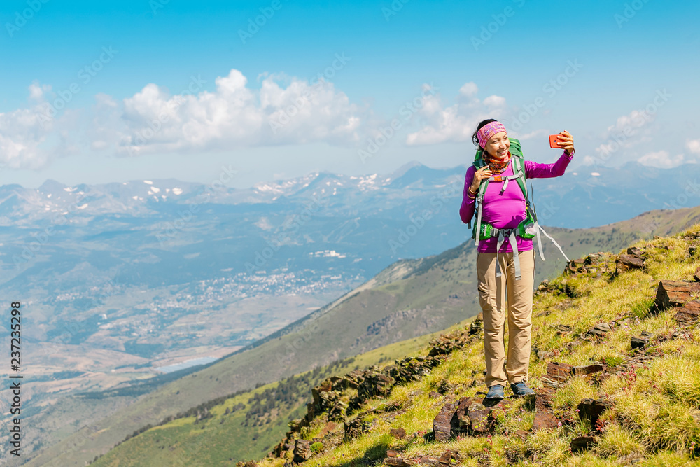 woman hiker taking photo with her smart phone on the top of the mountain peak