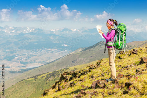Happy woman traveler with a backpack and a map on the background of the Pyrenees mountains. Hiking and adventure concept