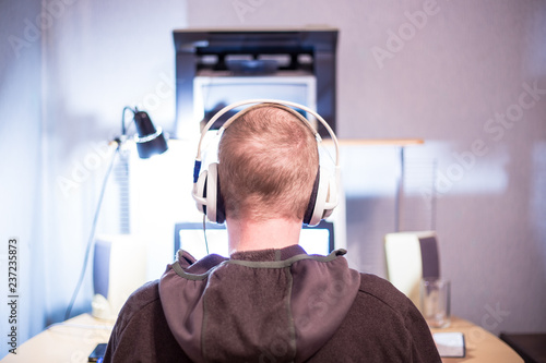 young man sitting in headphones at the computer, the view from the back