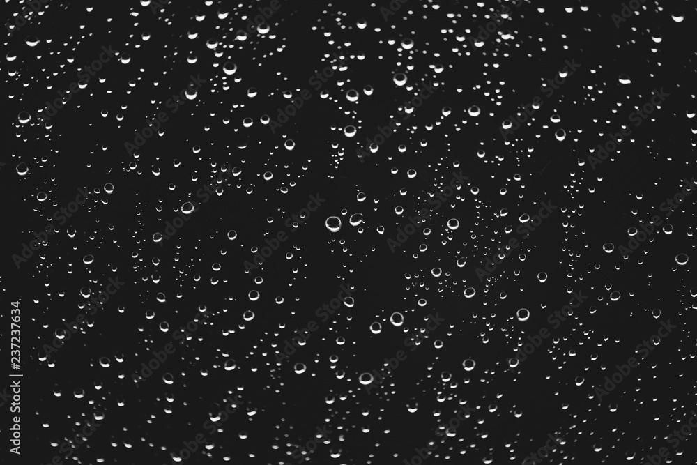 Dirty window glass with drops of rain. Atmospheric monochrome dark background with raindrops. Droplets and stains close up. Detailed transparent texture in macro with copy space. Rainy weather.