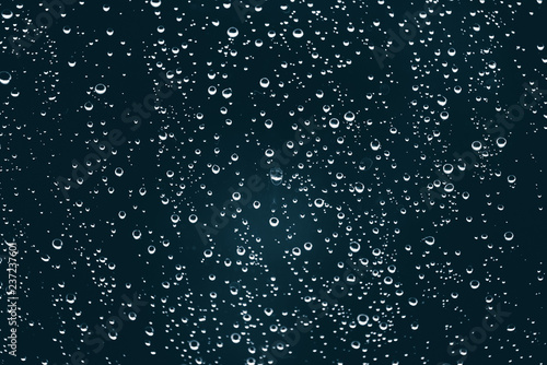 Dirty window glass with drops of rain. Atmospheric blue background with raindrops. Droplets and stains close up. Detailed transparent texture in macro with copy space. Rainy weather.