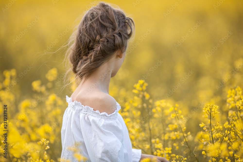 A girl in a white dress is standing on a flowering rapeseed field on a sunny day. A girl in a white dress is standing on a flowering rapeseed field on a sunny day.