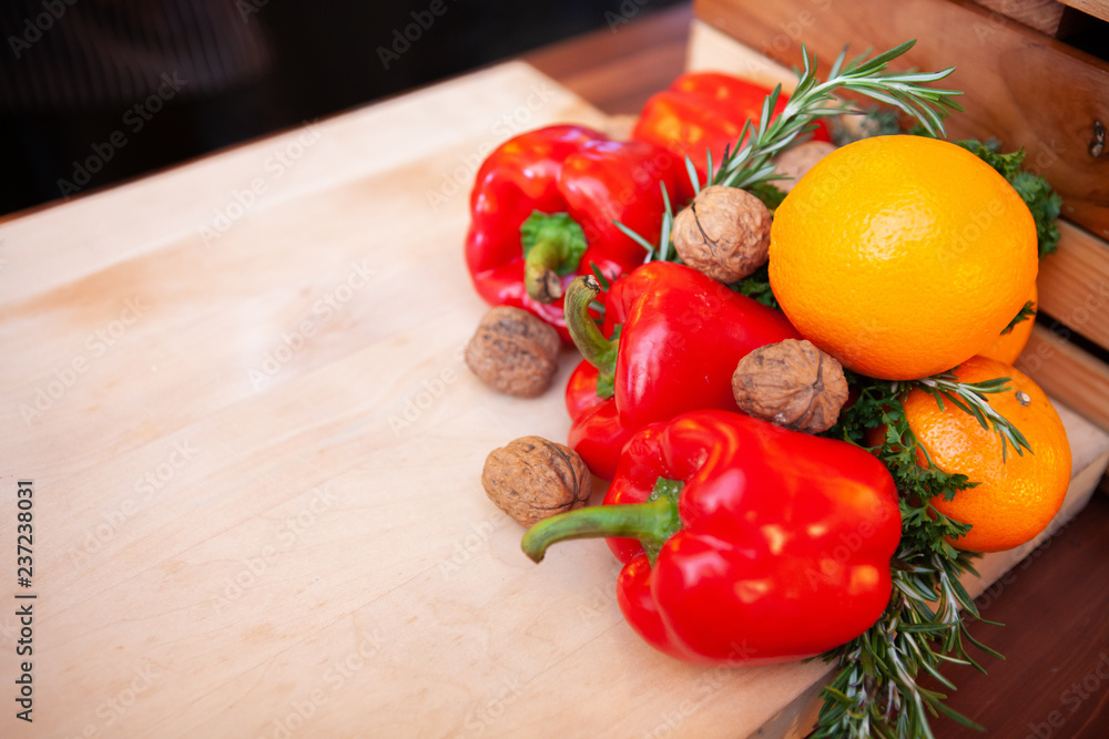 Assortment of fresh, raw vegetables for cooking. Colorful red bell peppers or ‎Capsicum and Orange fruit with Walnuts and Rosemary herbs on a chopping board with copy space. Selective focus. Close up.