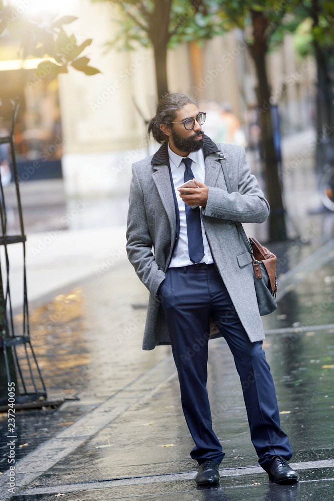 Businessman walking in the street, using smartphone
