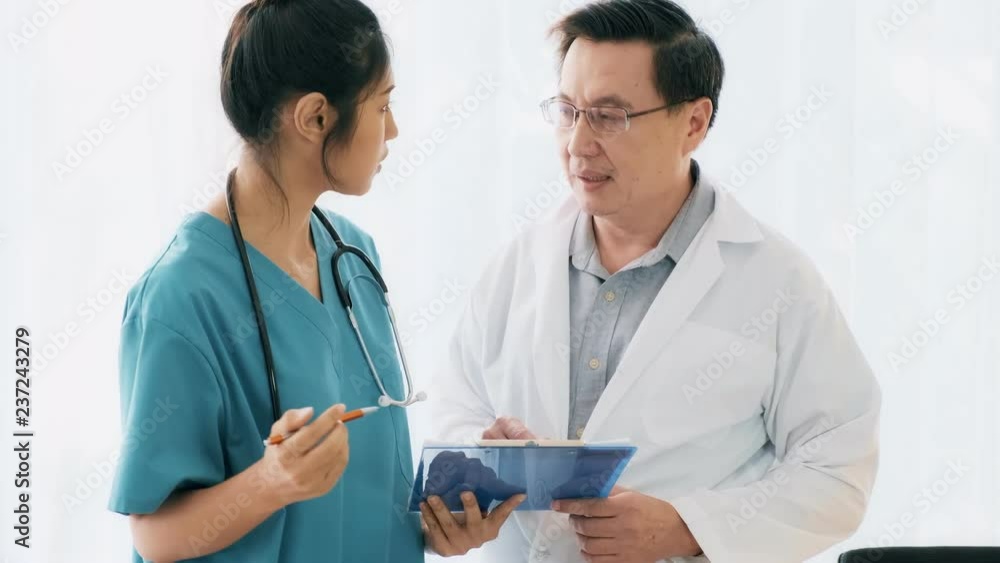 Senior asian man medical doctor standing, talking to young medical woman doctor examine her notes. Young medical doctor career concept. Senior asian man medical doctor standing, talking to young medical woman doctor examine her notes. Young medical doctor career concept.