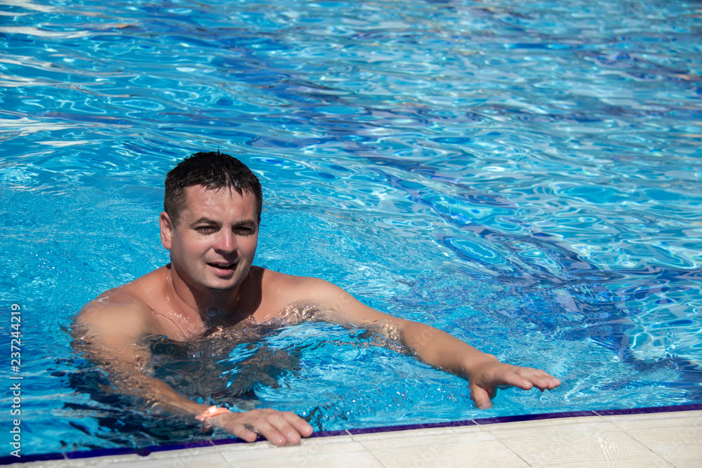 Man swimming in the pool. Positive handsome guy resting in the pool at summer day.