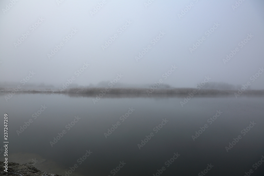 Thick morning fog over a narrow river in winter