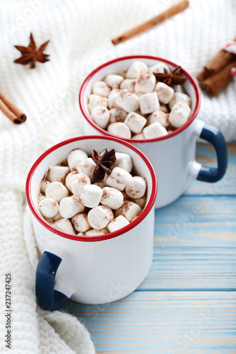 Cappuccino with marshmallows in mugs and knitted scarf on wooden table