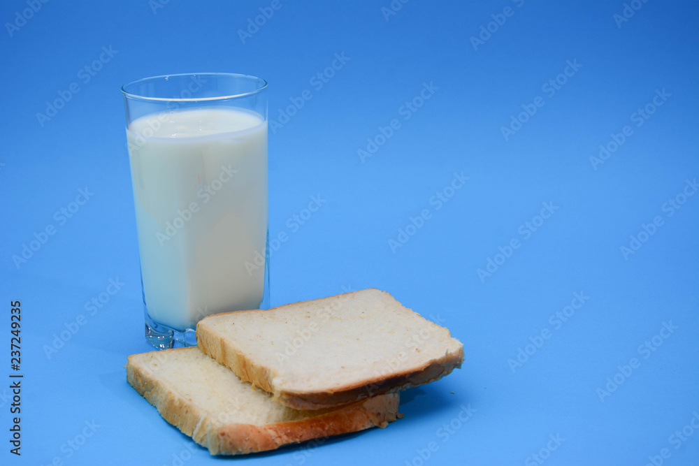 A glass of milk with a toasted bread on a pastel blue background. Two Bread Slices on blue background. Natural healthy food and organic farming concept. Copy space. A glass of milk with a toasted bread on a pastel blue background. Two Bread Slices on blue background. Natural healthy food and organic farming concept. Copy space.