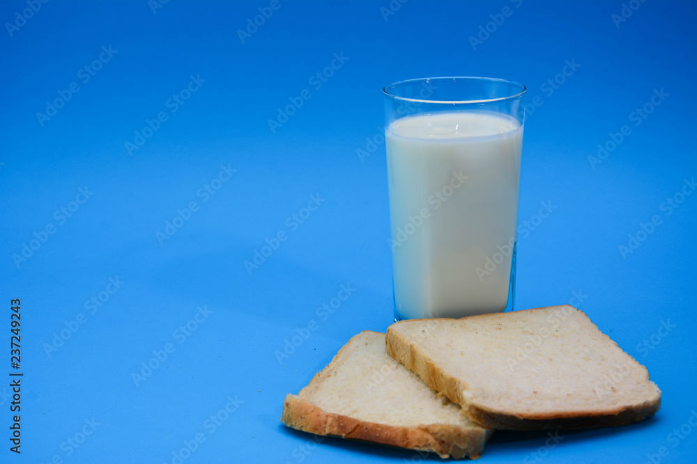 A glass of milk with a toasted bread on a pastel blue background. Two Bread Slices on blue background. Natural healthy food and organic farming concept. Copy space. A glass of milk with a toasted bread on a pastel blue background. Two Bread Slices on blue background. Natural healthy food and organic farming concept. Copy space.