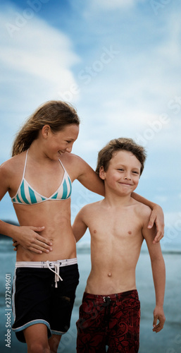 Teenage girl and her brother standing on a beach hugging. photo