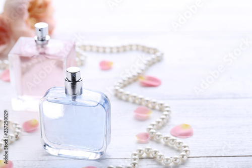 Perfume bottles with flower petals and beads on wooden table
