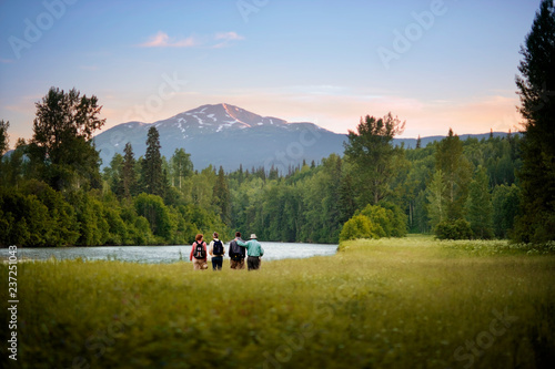 people hike along a river in a grassy field