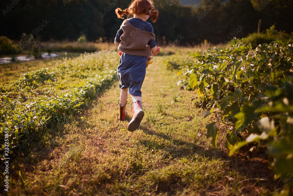 Young girl running between plants in a garden. Young girl running between plants in a garden.