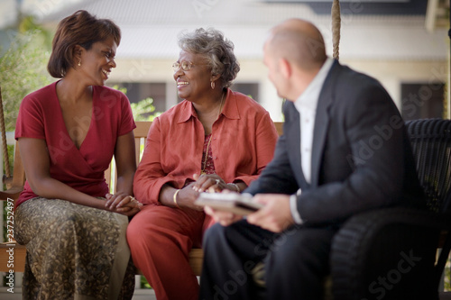 Mid-adult woman and her mature mother sitting on a porch with a male friend.