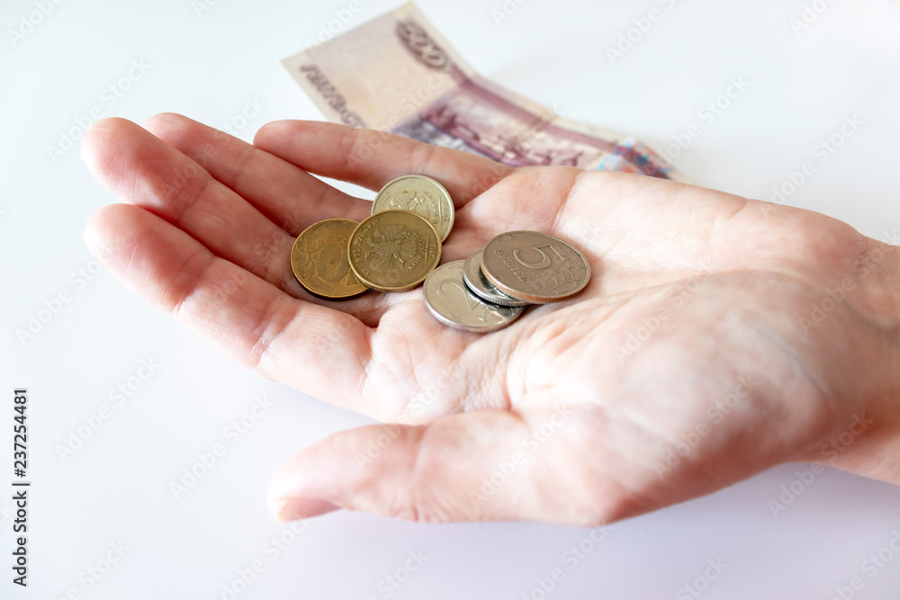Female hand holding a coin, coins and russian rubles on the table Female hand holding a coin, coins and russian rubles on the table