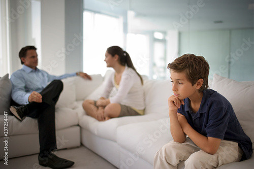 Boy sitting apart from his family on a sofa.