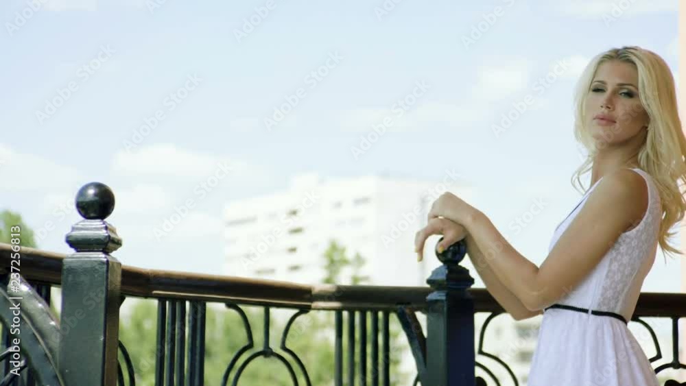 Young beautiful blonde woman posing on movie camera, standing on the balcony of a luxurious house. Slow motion. HD Young beautiful blonde woman posing on movie camera, standing on the balcony of a luxurious house. Slow motion. HD