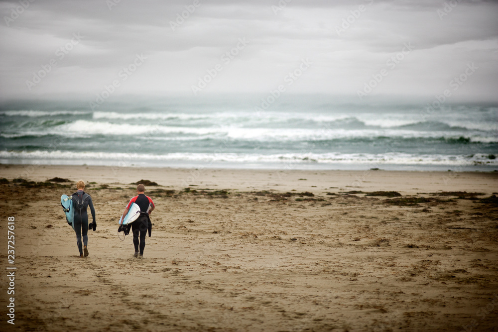 Two teenage boys holding surfboards walking across a beach. Two teenage boys holding surfboards walking across a beach.